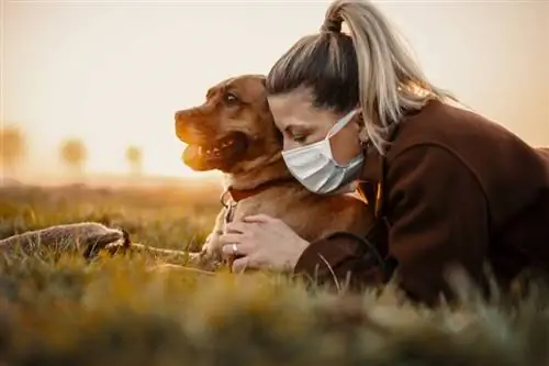 Mulher com máscara protetora caminha sozinha com cachorro ao ar livre por causa da pandemia do vírus corona