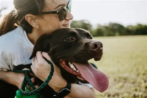 vrou wat haar sjokoladebruin hond omhels