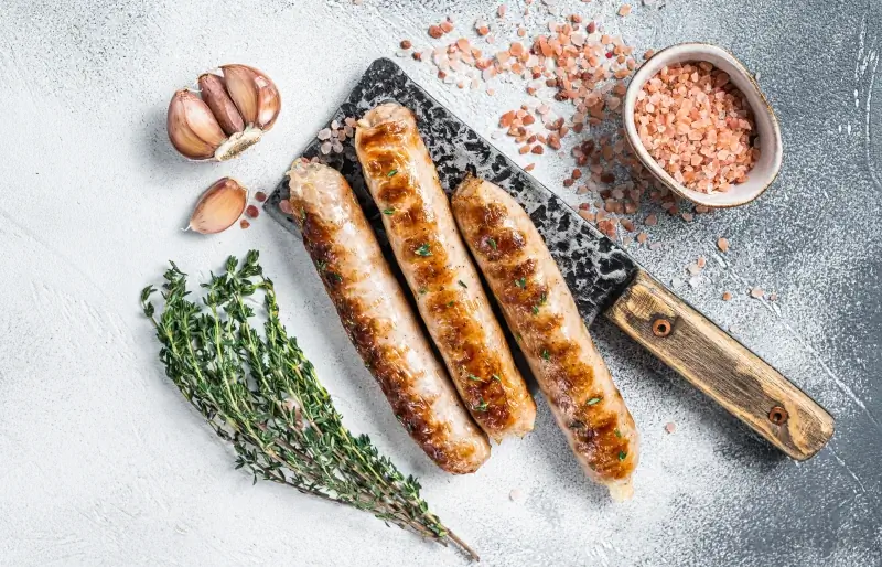 grilled bratwurst sausages rau ntawm lub cleaver nrog qej, ntsev thiab rosemary