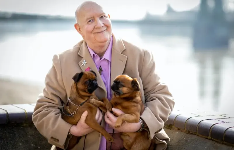 hombre mayor sosteniendo dos pugs de albaricoque en sus brazos