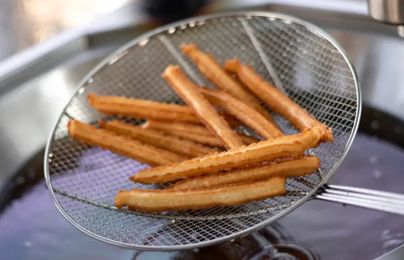 churros fraîchement frits sur une passoire en acier inoxydable